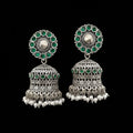 Pair of silver and green earrings on a gray stand with a blurred background