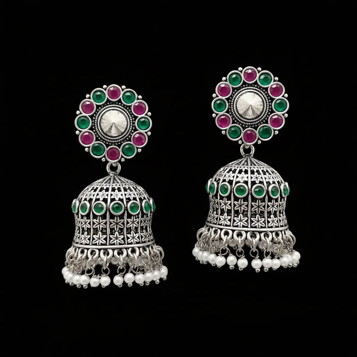 Pair of silver jhumka earrings with colorful gemstones and pearl accents on a gray stand.