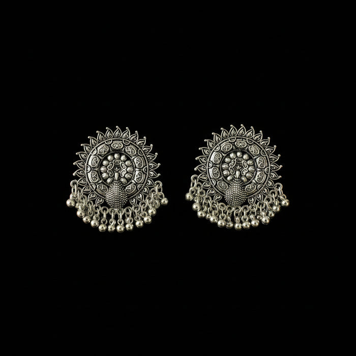A pair of ornate silver-toned Indian jhumka earrings with intricate filigree work, floral motifs, and dangling bead chains, displayed on a dark reflective surface.
