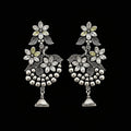 Silver floral earrings on a gray stand with 'Saheli' branding.