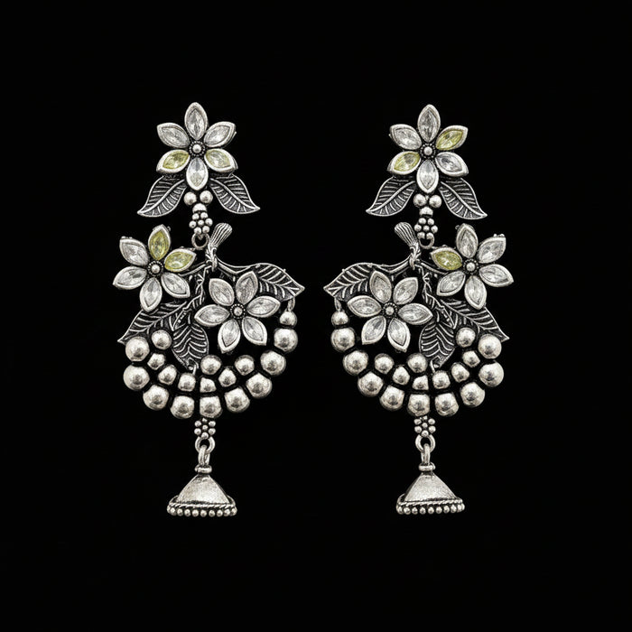 Silver floral earrings on a gray stand with 'Saheli' branding.