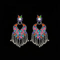 A pair of silver-toned Indian chandbali earrings decorated with vibrant pink, blue, orange, and green enamel, featuring dangling silver bells on a dark reflective surface.