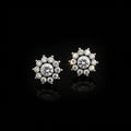 A pair of silver-toned stud earrings with clear round-cut gemstones arranged in a floral or snowflake-like cluster, displayed on a dark reflective surface with the SAHELI MY BEST FRIEND logo above.