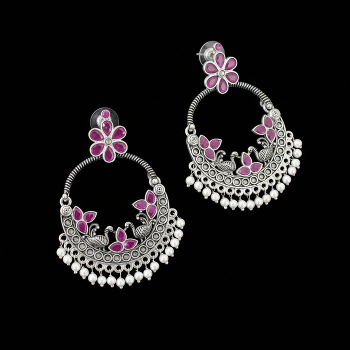 Ornate silver earrings with pink floral designs on a dark background