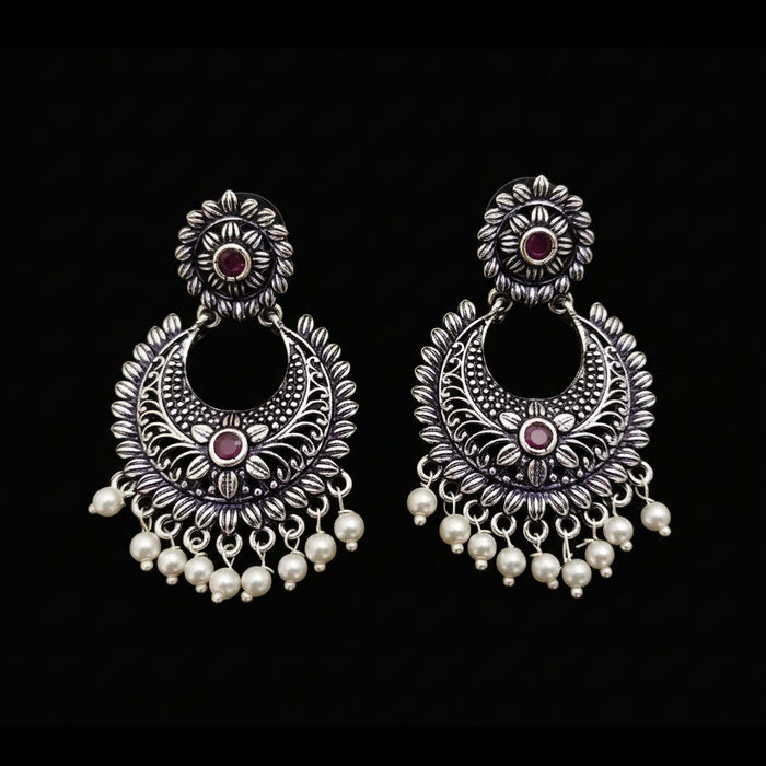 Pair of silver earrings with red stones and pearl drops on a gray background, branded 'Saheli'.