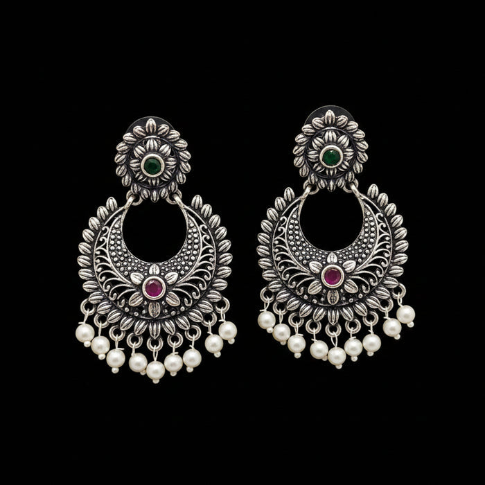 Pair of silver earrings with pearls and gemstones on a gray background, branded 'Saheli'.