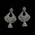 A pair of ornate silver-toned Indian jhumka earrings with intricate filigree work and dangling bead chains, displayed on a dark reflective surface.