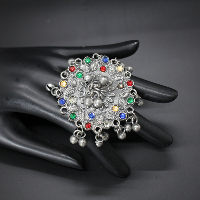 Decorative ring with multicolored gemstones on a black mannequin hand against a dark background