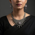 Silver necklace and earrings with 'Saheli' branding on a gray background