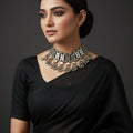 Silver necklace with dangling beads on a black background, featuring the brand 'Saheli'.