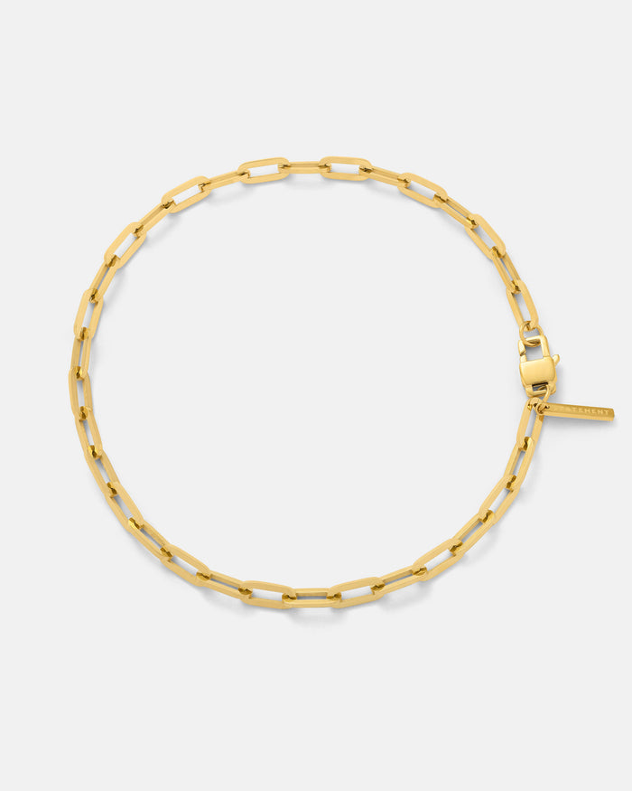 The Paperclip Chain (Gold) is an 18k gold plated bracelet with elongated rectangular links and a clasp, shown in a circular shape on a plain white background.