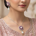 Jewelry set with pink gemstones and pearl drops on a dark background, featuring the brand 'Saheli'.