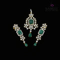 Ornate earrings with green gemstones and gold accents on a dark background, featuring the brand 'Saheli'.