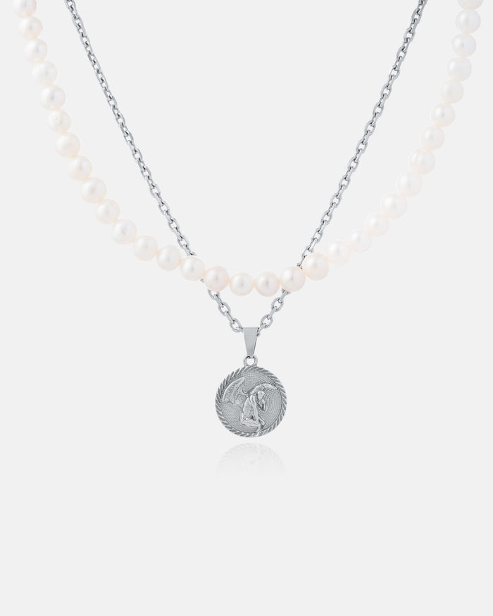 The Pearl Set (Custom Pendant Choice) features a freshwater pearl necklace with two strands—white pearls and a silver chain—and a round silver pendant engraved with a winged figure, shown on a plain white background.