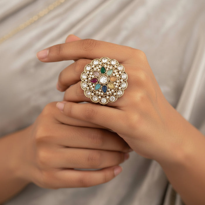 Gold-plated ring with a highly detailed, circular mandala-style filigree design, featuring clear stones and colorful enamel accents in green, blue, pink, orange, and yellow. Shown from both front and back views on a split beige and white background.