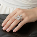 Silver floral ring on a black hand with 'SAHELI' branding.