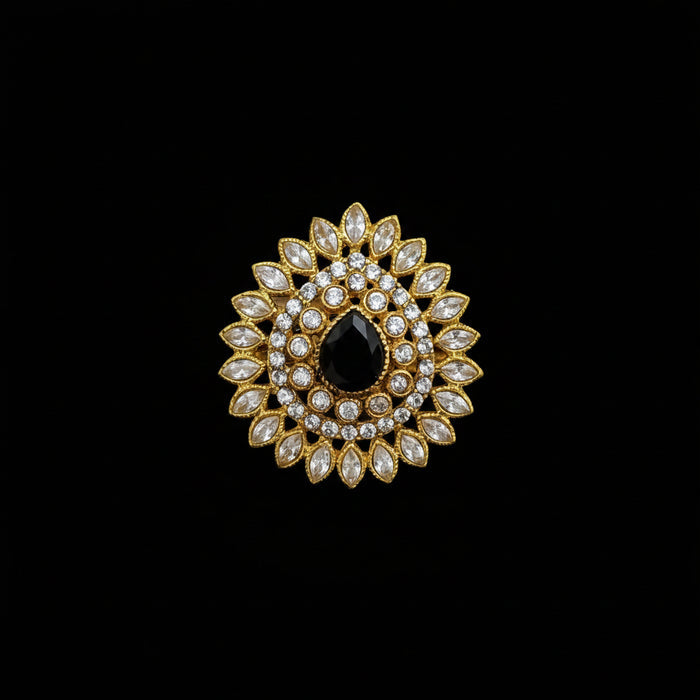 A gold-toned floral brooch featuring a central black teardrop-shaped stone surrounded by clear marquise and round crystals, displayed on a dark reflective surface with the SAHELL MY BEST FRIEND logo in the top left corner.