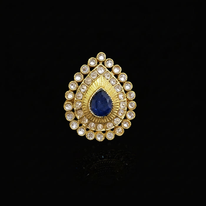 A gold teardrop-shaped ring with a central deep blue teardrop gemstone and surrounding clear rhinestones, displayed on a reflective gray surface. The brand logo 'SAHELI MY BEST FRIEND' is visible in the top left corner.