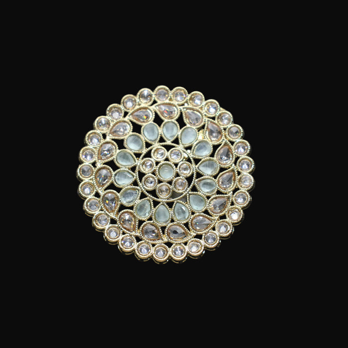 Gold and gemstone brooch on a black mannequin hand against a dark background