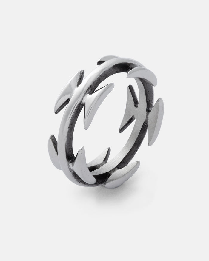 Introducing the Razor Wire Ring by Statement Collective—a striking piece of streetwear jewelry crafted in silver. This ring features evenly spaced, curved, thorn-like spikes that extend outward from both the inner and outer edges, creating a bold and edgy look that commands attention. Displayed against a plain white background.