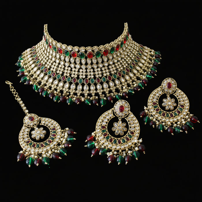 Ornate gold jewelry set with green and red stones on a dark background, featuring the brand 'Saheli'.
