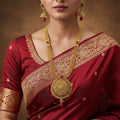 Gold necklace with red stones and matching earrings on a black background, branded 'Saheli'.