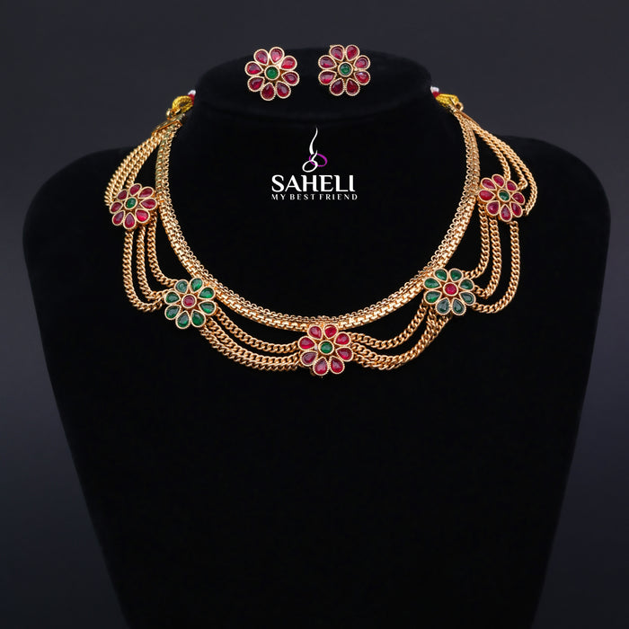 Gold necklace with floral designs and matching earrings on a black stand with 'SAHELI' branding.