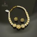 A gold and white beaded necklace with matching flower-shaped stud earrings, displayed on a dark reflective surface. The necklace features white pearl-like beads separated by gold spacer rings and three larger gold flower motifs with clear stones.