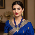 A royal blue beaded necklace and matching earrings set with gold-plated metal and white stones, displayed on a dark gray reflective surface. The brand logo 'SAHELI MY BEST FRIEND' is visible in the top right corner.