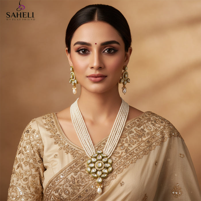 Gold-plated jewelry set featuring a multi-strand necklace and matching earrings with white faux pearls and clear stones, displayed on a dark reflective surface. The brand logo 'SAHELI JEWELLERY' is visible in the upper left.