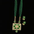 Green beaded necklace with a rectangular green and gold pendant, accompanied by matching earrings, displayed on a dark reflective surface. The brand logo 'SAHELL' is visible in the top right corner.
