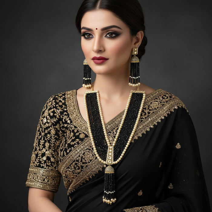A traditional Indian jewelry set featuring a long beaded necklace and matching earrings. The necklace has multiple strands of black beads accented with cream-colored pearl-like beads and gold-toned metal details, ending in dangling tassel-like clusters of black and cream beads.
