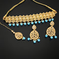 Gold-toned Indian bridal jewelry set featuring a choker necklace, matching earrings, and a maang tikka, embellished with white stones and light blue bead accents, displayed on a dark reflective surface with the SAHeli brand logo.