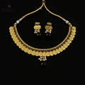 Gold coin necklace and matching earrings with black beads and white pearl accents, displayed on a dark reflective surface. The SAHeli by Saheli brand logo is visible in the top left corner.