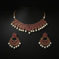 Gold-plated Indian traditional jewelry set featuring a choker necklace and matching earrings, embellished with pinkish-red enamel, white faux pearls, and gold details, displayed on a dark reflective surface.