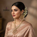 Gold-toned traditional Indian jewelry set including a necklace and matching earrings with intricate filigree work and dangling pearl-like beads, displayed on a dark reflective surface. The brand name 'SAHELL MYSTERY STORE' is visible in the upper left.