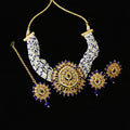 Gold and white beaded Indian jewelry set including a statement necklace, matching earrings, and a maang tikka, displayed on a dark gray background with the Saheli brand logo.