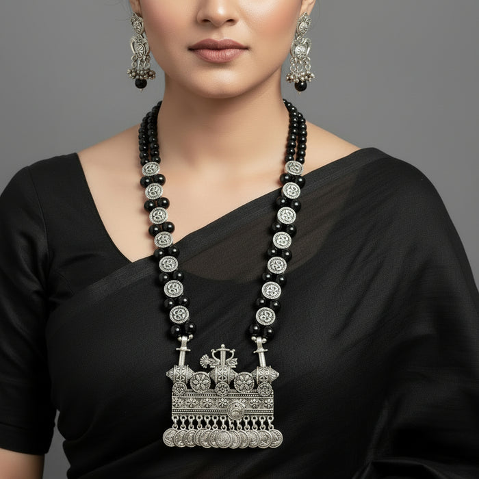 Black beaded necklace with silver pendant and earrings on a gray background, featuring the brand 'Saheli'.