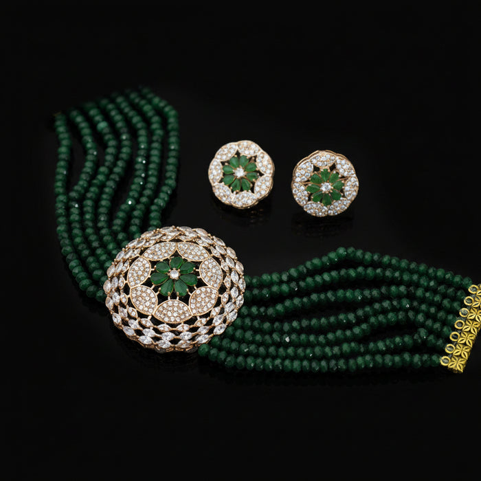 Green beaded necklace with gold and diamond earrings on a dark background