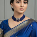 Blue beaded necklace and earrings set with gold accents on a reflective surface, featuring the brand 'Saheli'.