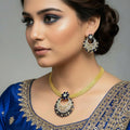 Gold necklace with matching earrings on a dark background, featuring the brand 'Saheli'.