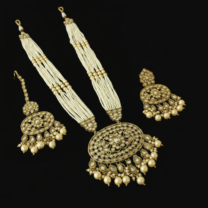 Ornate gold and pearl necklace with matching earrings on a reflective black surface