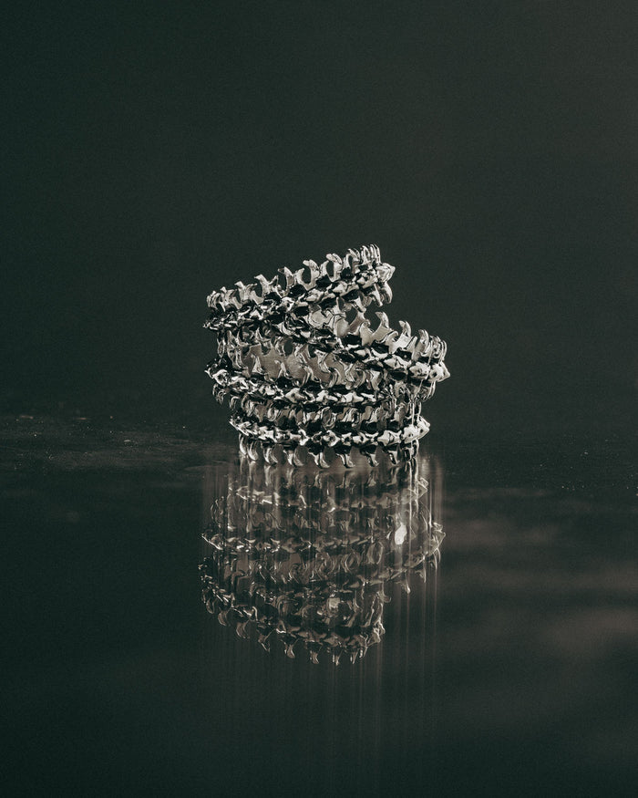 Stack of silver bone rings on a reflective black surface with a dark background