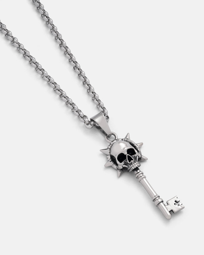 Silver key-shaped pendant with skull design on a chain against a white background