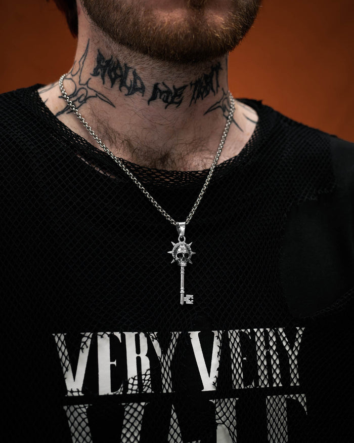 Silver key-shaped pendant with skull design on a chain on tattooed model's neck