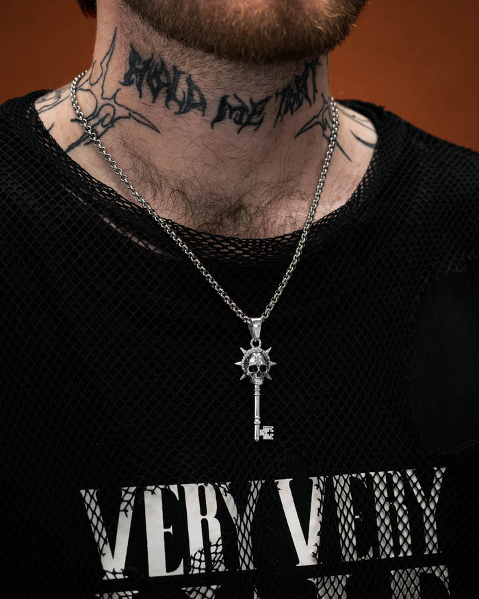 Silver key-shaped pendant with skull design on a chain on tattooed model's neck by statement collective
