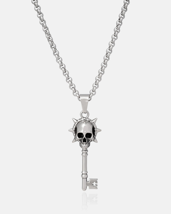 Silver key-shaped pendant with skull design on a chain hanging against a white background