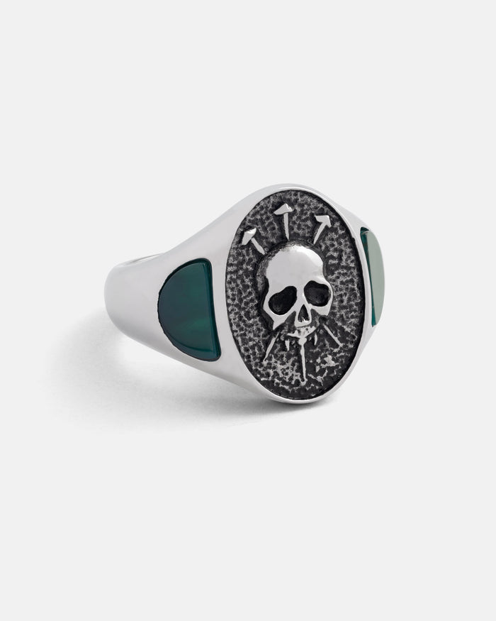Silver ring with skull design and green stones on a white background