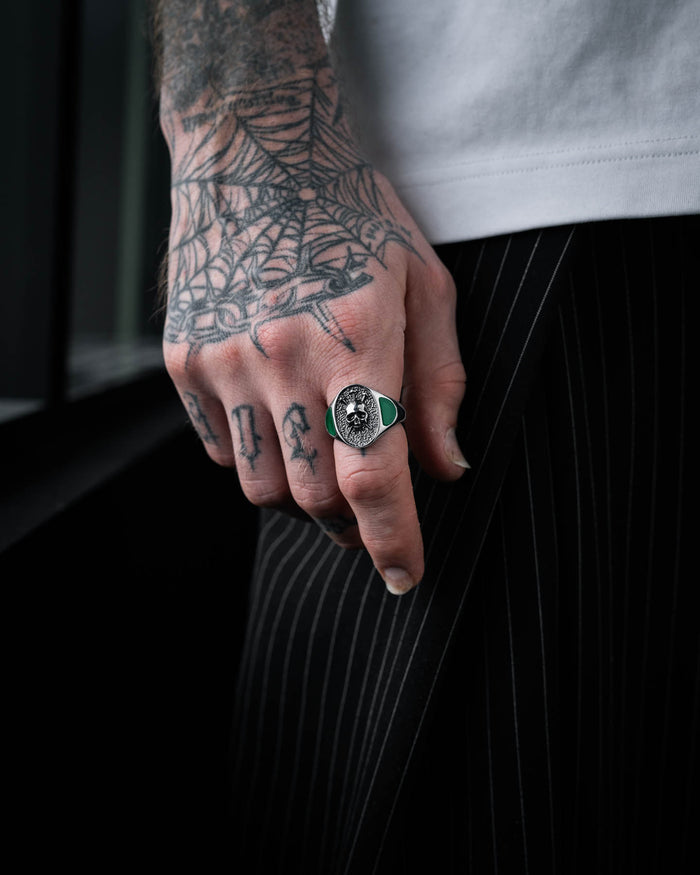 signet ring with skull and green stones on tattooed mans hand