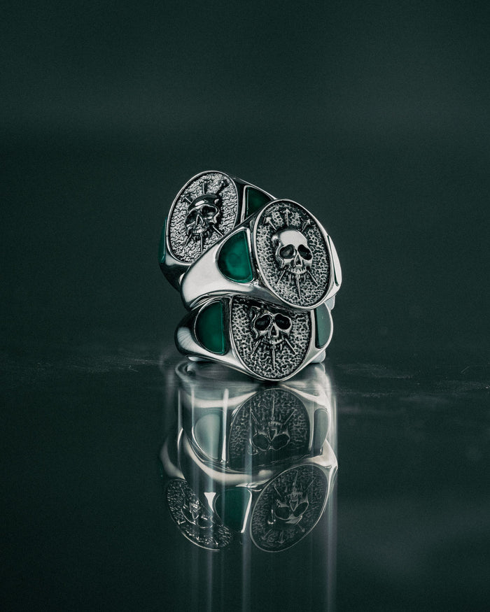 Silver skull ring with green gemstone on a reflective surface with dark background